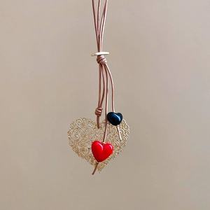 Detail of hollow gold heart pendant with red and black charms on brown leather cord