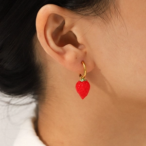 Close-up of a gold hoop earring featuring a red strawberry pendant on a model's ear