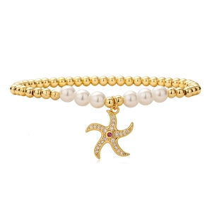 Détail d'un bracelet en perles dorées avec un pendentif étoile de mer serti de zircons