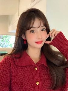 Detail of red festive earrings with bow and Chinese plaque on a red knit cardigan