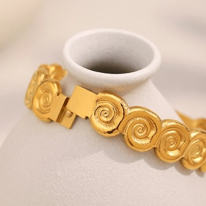 Macro detail of 18K gold plated conch shell bracelet with spiral texture on white vase