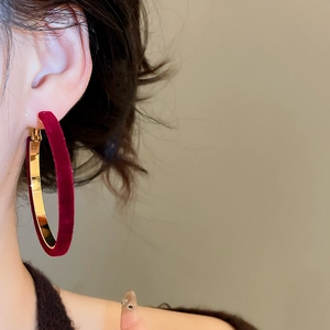 Close-up of elegant burgundy velvet and gold metal hoop earring worn by a model