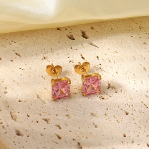 Close-up of pink square zircon earrings with gold plating on textured stone and silk