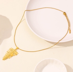 Detailed close-up of golden leaf pendant with extension chain on a white ceramic plate