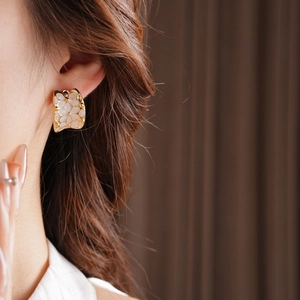 Détail d'une boucle d'oreille florale en forme de C plaquée or portée avec un éclairage chaud