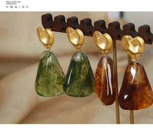Macro detail of heart studs with green and amber resin teardrop pendants on wood stand