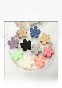 Flat lay of 11 matte flower hair claws in various Morandi colors on a white ceramic plate