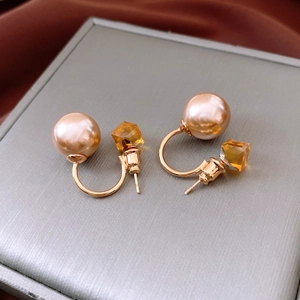 Détail de boucles d'oreilles en U avec perle champagne et cristal ambré sur fond gris