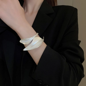 Detailed view of matte silver leaf-shaped cuff bracelet on model with black blazer
