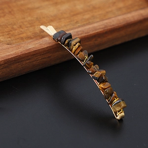 Detailed close-up of a golden hair clip featuring raw tiger eye crystal stones on a dark wood background