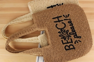 Détail de cabas en paille tissée beige et marron avec broderie Beach please décorée