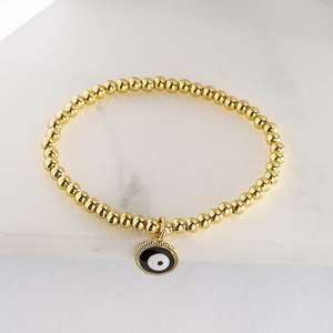 Gold beaded stretch bracelet featuring a black and white enamel Evil Eye charm on marble