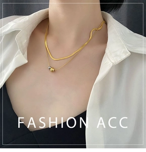 Detail of layered gold snake chain and silver bead necklace on a model wearing white shirt