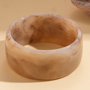 Detailed top view of a wide resin bangle with amber marble texture on warm matte background