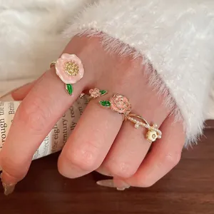 Ensemble de trois bagues dorées à motifs floraux en émail rose et perles blanches