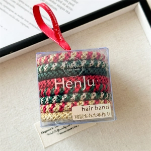 Close-up of colorful braided Christmas hair ties in a clear gift box with silk handle