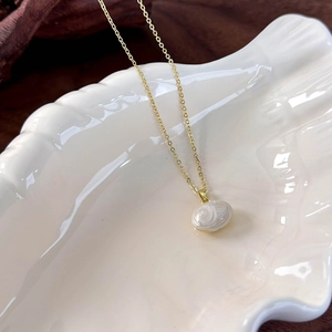 Detail view of a minimalist cream bean pendant on a delicate gold chain in a shell dish