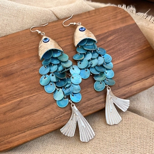 Detail of fish-shaped earrings with blue sequin scales and evil eye on rustic wood