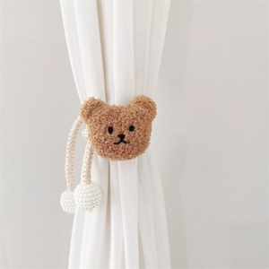 Detail of plush brown bear curtain tieback with woven rope and elegant pearl pendant