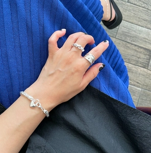 Detail of twisted rope ring and heart charm bracelet worn by a model in silver finish