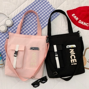 Detail of canvas tote bags with 'NICE!' lettering and buckle pockets in pink and black