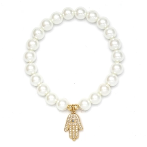 Macro detail of white pearl bracelet featuring a golden Hamsa Hand charm with blue crystal