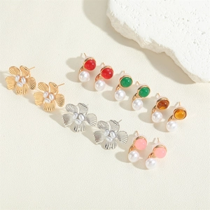 Flat lay of small acrylic flower earrings and pearl stud set on a beige textured background