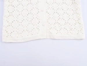 Detail of white crochet knit cardigan hem and delicate buttons on a flat lay background