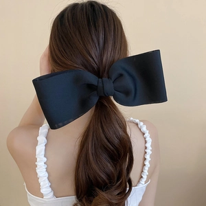 Detail view of a large black silk bow hair clip worn on wavy brown hair for an elegant look