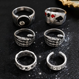 Detailed view of silver Gothic rings featuring skull and poker motifs on a black glitter base