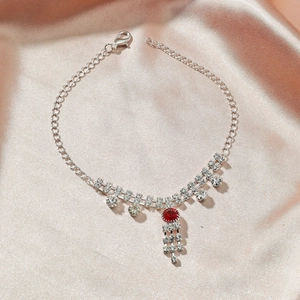 Détail macro d'une chaîne de cheville argentée avec strass rouge et pampilles brillantes