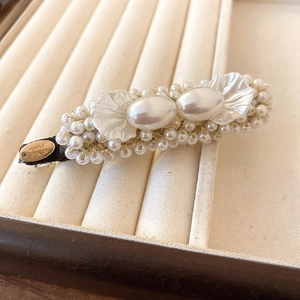 Detailed macro view of imitation pearl flower hair clip with a gold Hand Made metal tag
