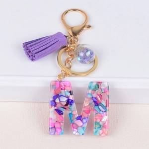 Resin initial M keychain with purple tassel and colorful stones on a white background