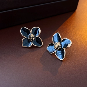 Gros plan de boucles d'oreilles fleurs dorées avec émail bleu foncé sur cuir