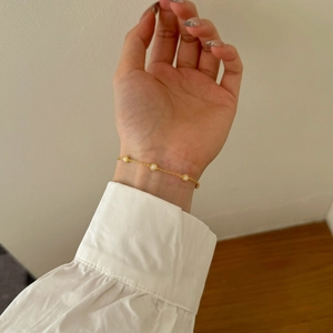 Elegant gold Mobius bracelet with round white stones worn on wrist against a wooden table