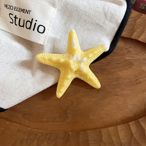 Detailed close-up of a yellow starfish hair clip with realistic textures on a wooden tray