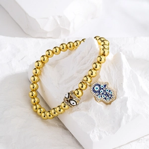 Golden Hamsa Hand and Evil Eye beaded bracelet displayed on a white textured stone base