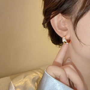 Close-up detail of French style C-shaped pearl earring with green zircon on model's ear