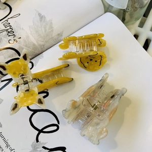 Detailed view of dog-shaped acetate hair claw clips on an artistic magazine background