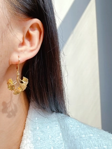 Close-up of golden ginkgo leaf earrings with brushed metal texture on a model