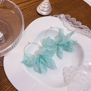 Dettaglio di orecchini a cerchio con fiori in tessuto azzurro su vassoio bianco