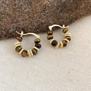 Macro shot of gold hoop earrings with brown gemstone beads on neutral fabric