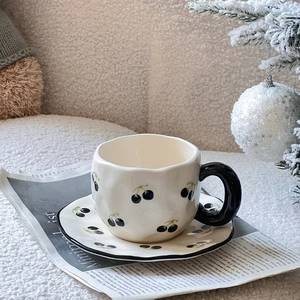 Close-up of a hand-painted ceramic coffee cup with cherry patterns on a newspaper