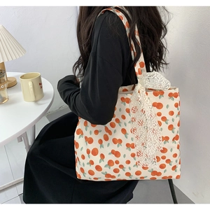 Canvas tote bag with orange fruit print and white lace bow detail shown on shoulder