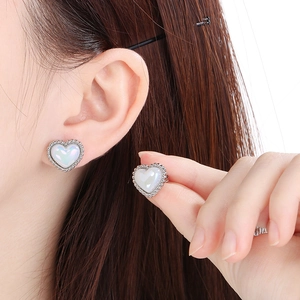 Close-up of heart-shaped pearlescent earrings with beaded silver edges on ear