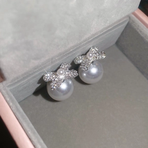 Macro view of bow-knot pearl earrings with sparkling diamonds on grey velvet box