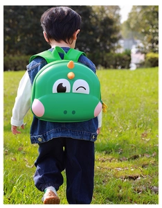 Macro shot of a green dinosaur hardshell backpack on a child in an outdoor park setting