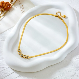 Golden snake chain necklace with five heart-shaped zircon pendants on a white stone tray