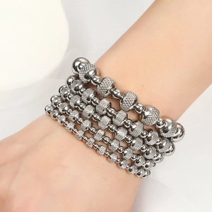 Close-up of five silver stainless steel beaded bracelets with various textures on a wrist