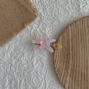Close-up of pink glitter starfish hair clip with pearl and rhinestone on a wooden base
